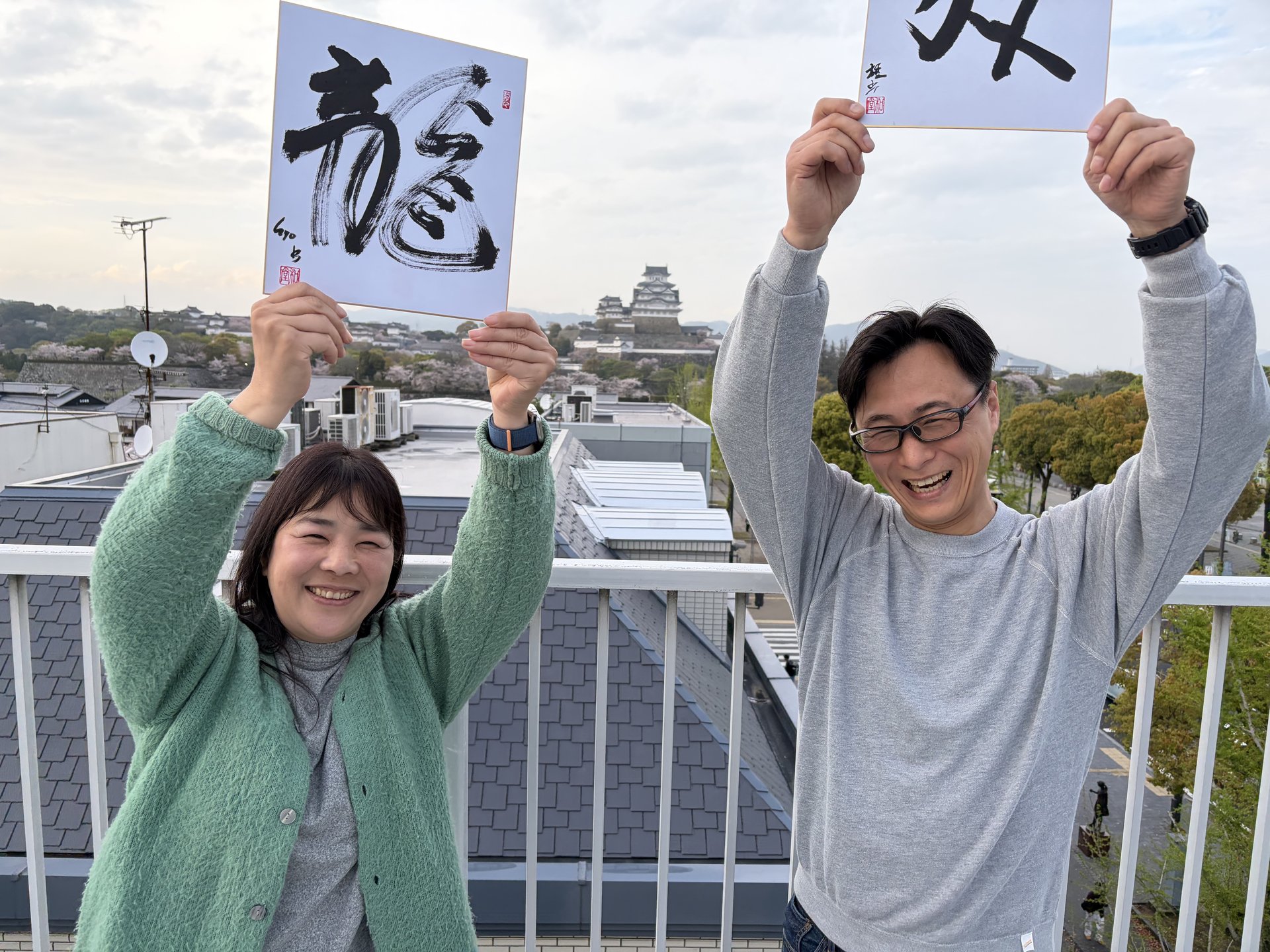 Guests holding finished calligraphy with Himeji Castle in the background